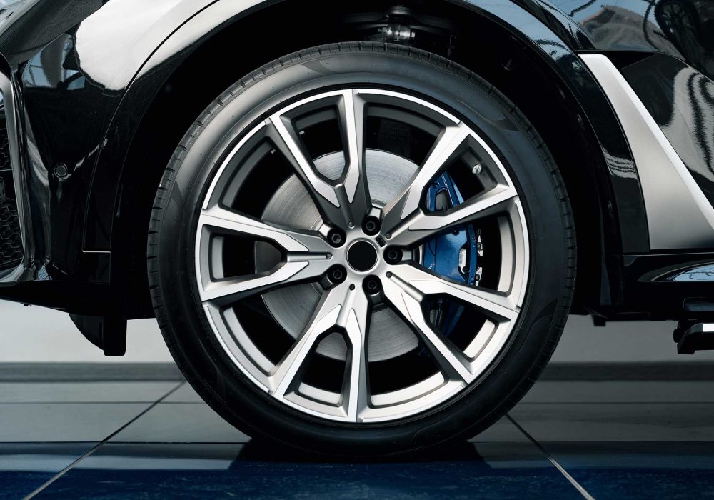 A close-up view of a stylish alloy wheel on a black car, showcasing its intricate design and shiny finish. The background features a smooth, reflective surface.