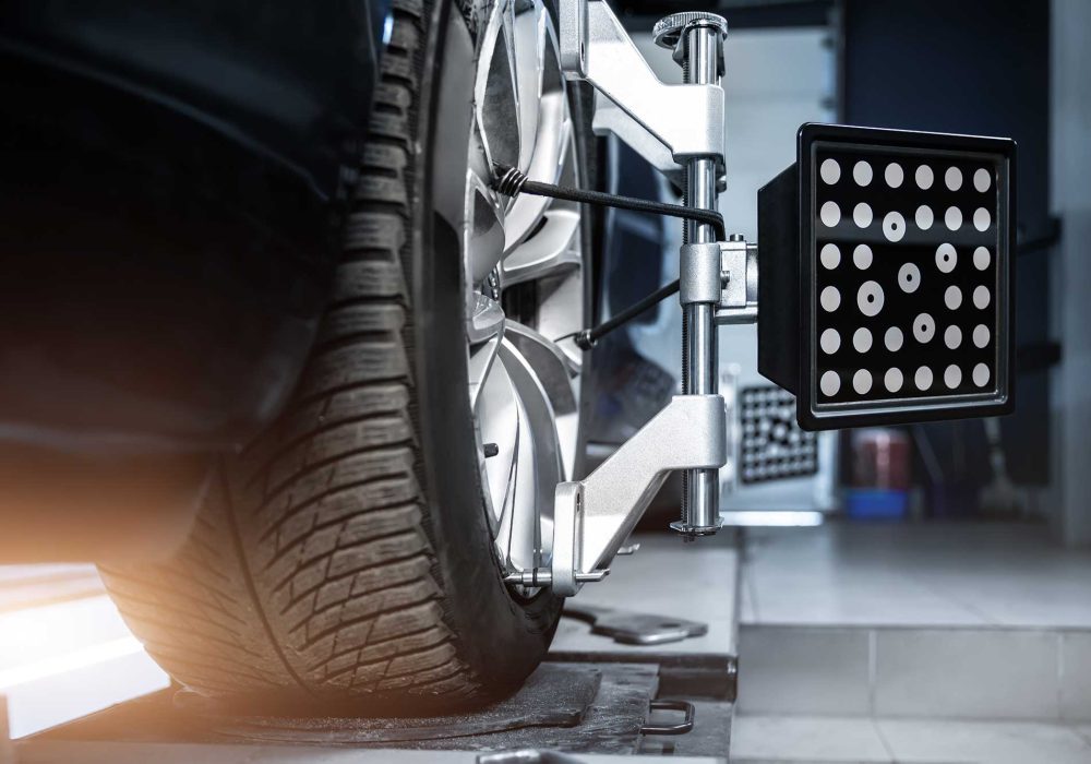 A close-up view of a car tire being aligned with a specialized machine, featuring a light panel and alignment tools. The setting appears to be an automotive workshop.