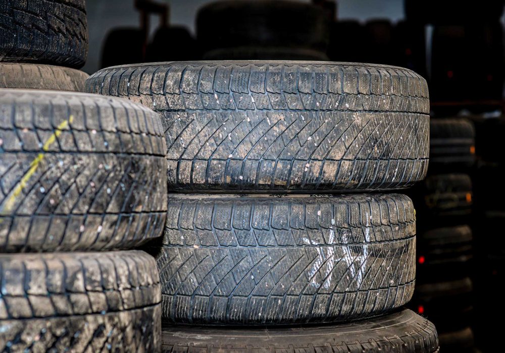 Stacked used tires in a storage area, showing worn tread patterns and dirt.